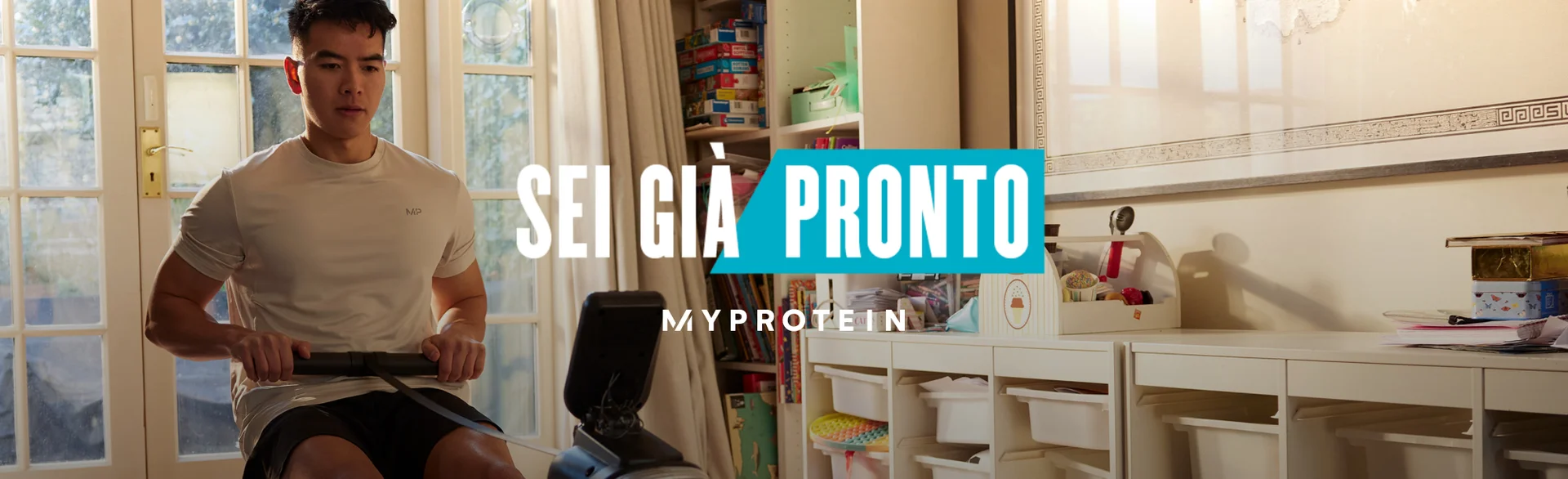Un uomo si allena su un vogatore a casa con le parole "Sei già pronto - MY PROTEIN" sovrapposte.